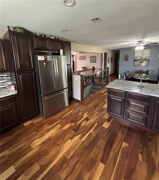 1205 W 14th Street Ct, Chanute, KS 66720 - kitchen with freestanding refrigerator, dark wood-style floors, dark brown cabinetry, a ceiling fan, and light stone counters
