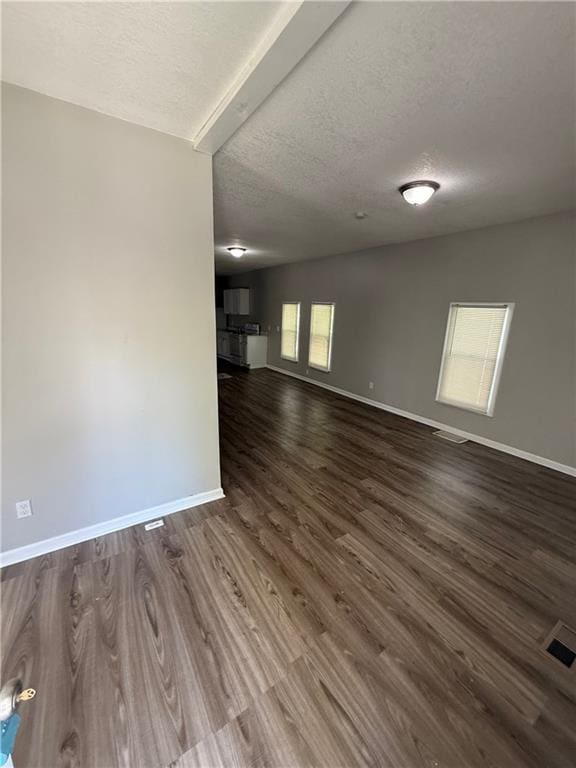 3318 E 24th St, Kansas City, MO 64127 - unfurnished living room with a textured ceiling, dark wood finished floors, and baseboards