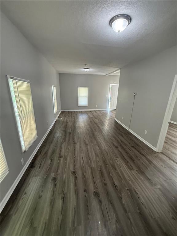 3318 E 24th St, Kansas City, MO 64127 - unfurnished room featuring dark wood-type flooring, baseboards, and a textured ceiling