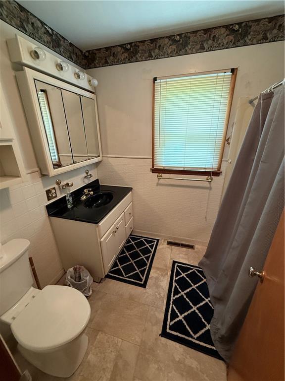 913 N Maple St, Stanberry, MO 64489 - full bath with tile walls, vanity, toilet, wainscoting, and a shower with shower curtain