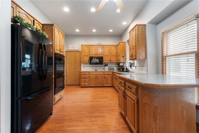 12484 S Hallet St, Olathe, KS 66062 - kitchen with black appliances, a peninsula, light wood-style floors, a sink, and light countertops