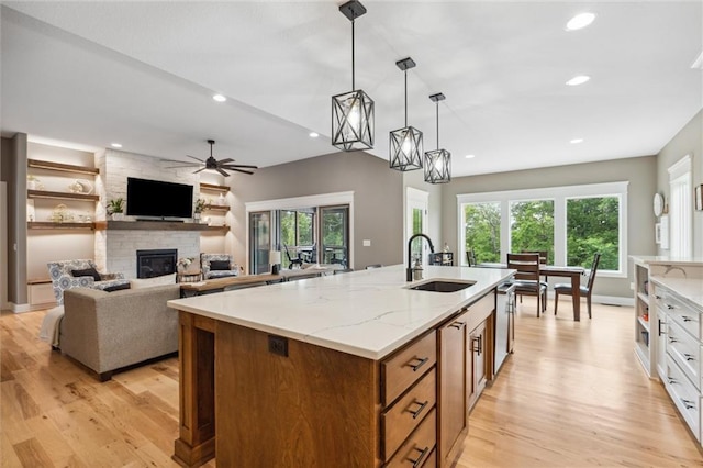 3112 Legacy Wood Dr, Lees Summit, MO 64086 - kitchen with a sink, brown cabinetry, light wood-style floors, a fireplace, and a kitchen island with sink