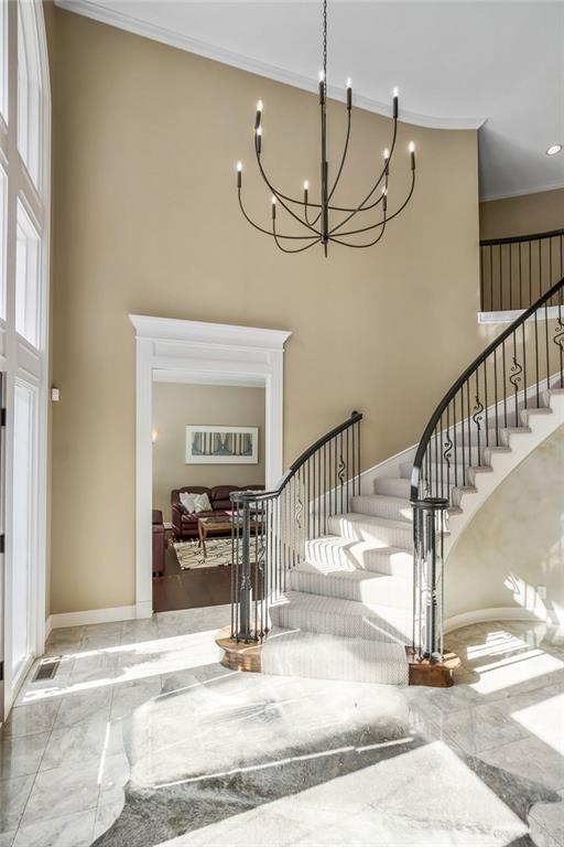 9705 Sunset Cir, Lenexa, KS 66220 - stairs featuring marble tiled floors, a chandelier, crown molding, a towering ceiling, and baseboards