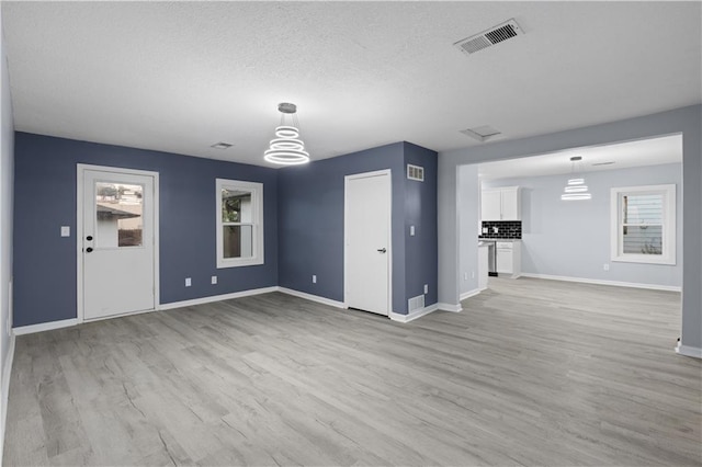 1709 Marty Ave, Kansas City, KS 66103 - unfurnished living room with baseboards, a chandelier, a textured ceiling, light wood-type flooring, and healthy amount of natural light