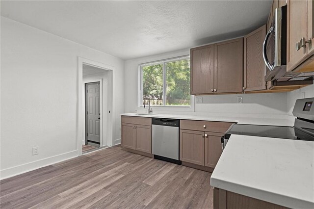 6 W 98th Ter, Kansas City, MO 64114 - kitchen featuring stainless steel appliances, a sink, light wood-type flooring, light countertops, and a textured ceiling