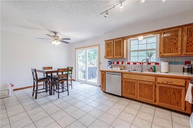 516 S St, Grain Valley, MO 64029 - kitchen with stainless steel dishwasher, brown cabinetry, light countertops, backsplash, and plenty of natural light