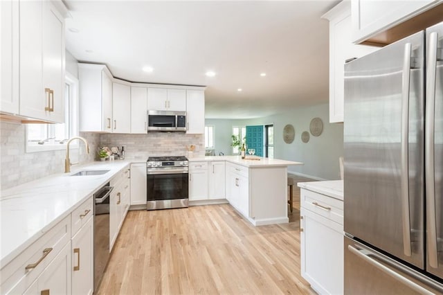 5308 Foster St, Overland Park, KS 66202 - kitchen featuring stainless steel appliances, a sink, a peninsula, light wood-type flooring, and decorative backsplash