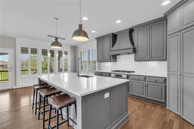 9812 Saddletop St, Lenexa, KS 66227 - kitchen with gray cabinets, custom exhaust hood, a center island with sink, decorative backsplash, and light countertops