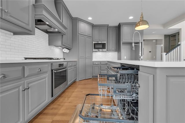 9812 Saddletop St, Lenexa, KS 66227 - kitchen with gray cabinets, appliances with stainless steel finishes, custom exhaust hood, recessed lighting, and light wood-style floors