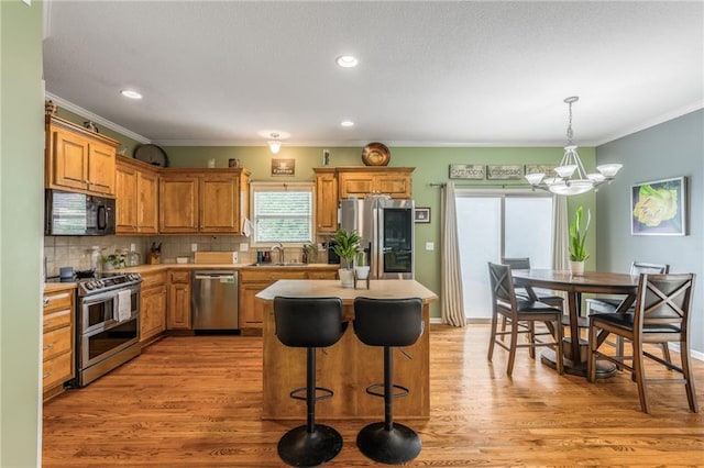 2420 SW Golden Eagle Rd, Lees Summit, MO 64082 - kitchen with stainless steel appliances, a chandelier, light wood-type flooring, ornamental molding, and brown cabinetry