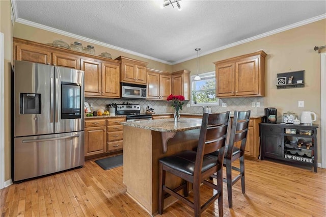 2436 SW Current Ln, Lees Summit, MO 64082 - kitchen with stainless steel appliances, brown cabinetry, light wood finished floors, a textured ceiling, and light stone counters