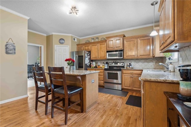 2436 SW Current Ln, Lees Summit, MO 64082 - kitchen with stainless steel appliances, brown cabinets, light wood-style floors, light stone counters, and ornamental molding