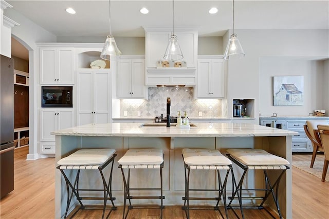 16394 S Loiret St, Olathe, KS 66062 - kitchen featuring black microwave, arched walkways, white cabinets, decorative backsplash, and light wood-style flooring