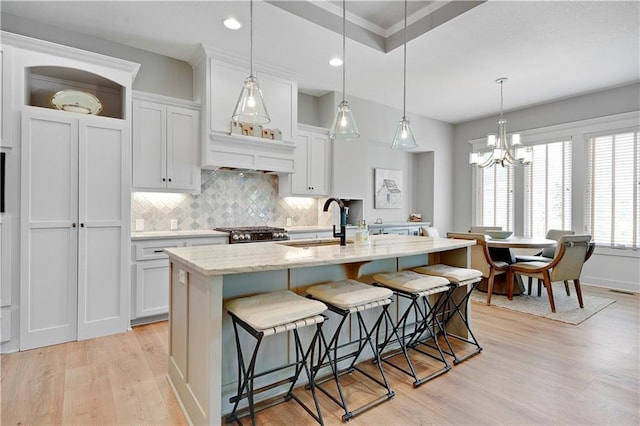 16394 S Loiret St, Olathe, KS 66062 - kitchen with light wood finished floors, a chandelier, decorative backsplash, a center island with sink, and a breakfast bar area