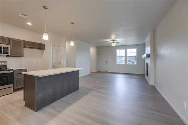 27027 E Oak View Dr, Lees Summit, MO 64086 - kitchen with appliances with stainless steel finishes, a fireplace, a ceiling fan, light countertops, and light wood-style flooring