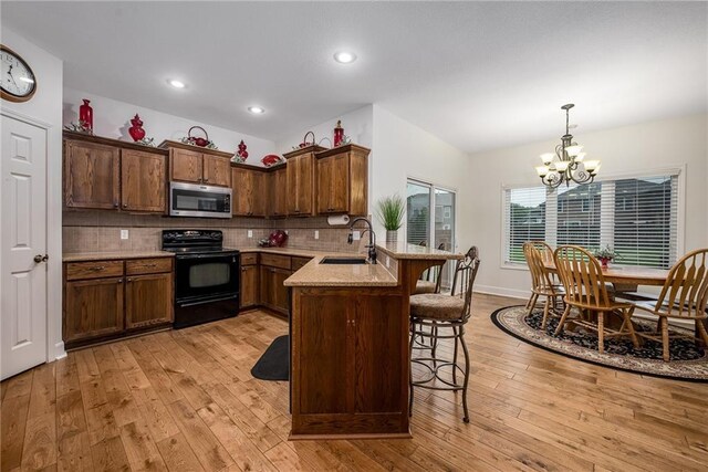 14165 Ashbury Ct, Basehor, KS 66007 - kitchen with electric range, stainless steel microwave, a sink, a chandelier, and light wood-type flooring