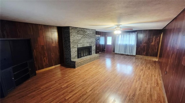 1045 Yale Rd, Mapleton, KS 66754 - unfurnished living room with wooden walls, a fireplace, wood finished floors, a ceiling fan, and a textured ceiling