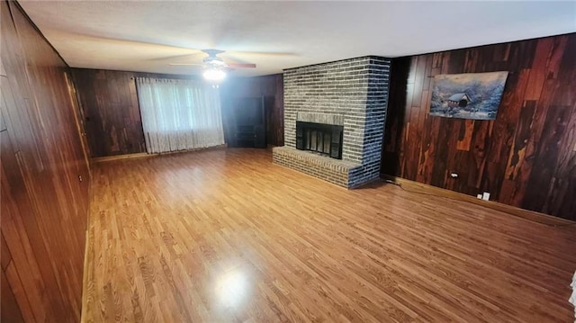 1045 Yale Rd, Mapleton, KS 66754 - unfurnished living room with wooden walls, a brick fireplace, a ceiling fan, and wood finished floors