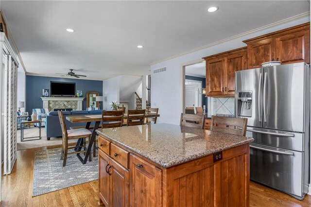 21222 W 46th Ter, Shawnee, KS 66218 - kitchen with stainless steel fridge with ice dispenser, a ceiling fan, a tiled fireplace, stone countertops, and a center island
