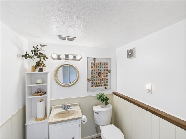8101 E 133rd Ter, Grandview, MO 64030 - half bath featuring toilet, wainscoting, vanity, a textured ceiling, and a decorative wall