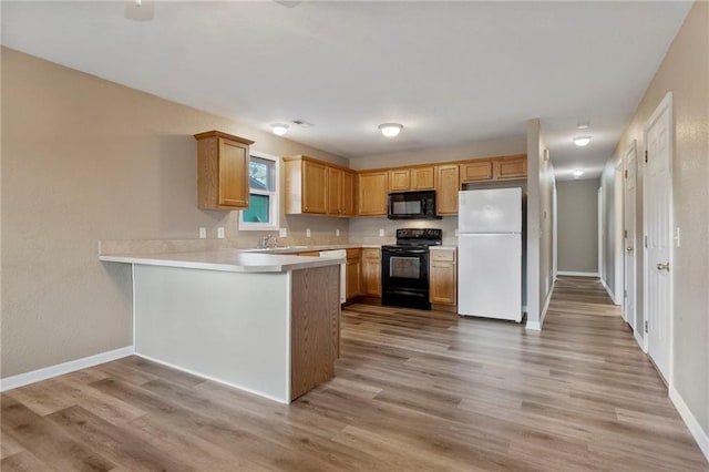 739 S Cypress St, Ottawa, KS 66067 - kitchen with black appliances, a peninsula, light wood-style flooring, and light countertops