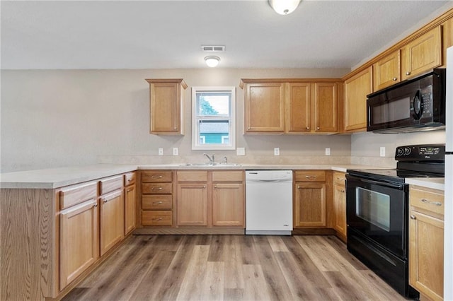 739 S Cypress St, Ottawa, KS 66067 - kitchen with black appliances, a peninsula, light wood-type flooring, and light countertops