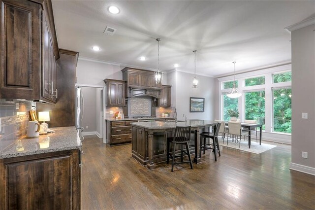 14095 NW 60th Ct, Parkville, MO 64152 - kitchen with decorative backsplash, an island with sink, dark brown cabinets, crown molding, and a kitchen breakfast bar