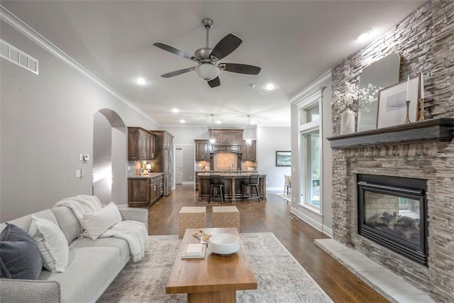 14095 NW 60th Ct, Parkville, MO 64152 - living area featuring a stone fireplace, a ceiling fan, dark wood-style flooring, crown molding, and arched walkways