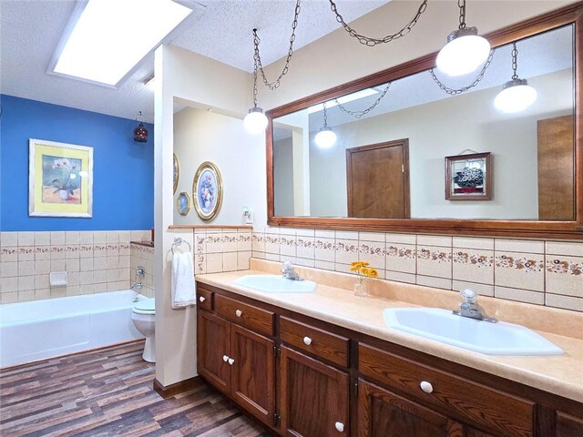 2101 Hillview Rd, Liberty, MO 64068 - full bathroom with wood finished floors, double vanity, tile walls, a garden tub, and a textured ceiling