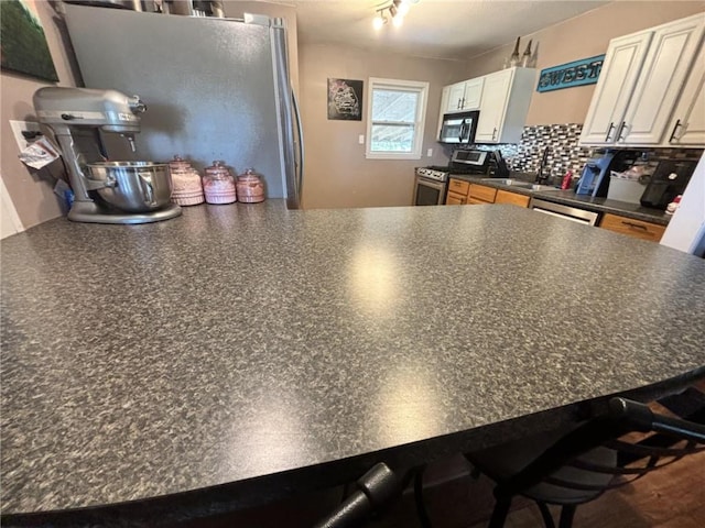 32592 SE 500th Rd, Kincaid, KS 66039 - kitchen featuring stainless steel appliances, dark countertops, a peninsula, decorative backsplash, and white cabinets