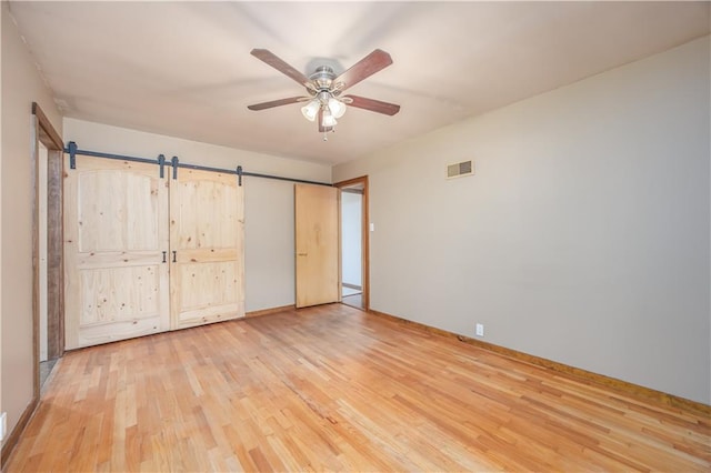 3931 Main St, Parsons, KS 67357 - unfurnished bedroom featuring light wood-style flooring, baseboards, a barn door, and ceiling fan