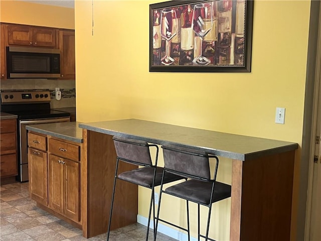 8425 N Tracy Ave, Kansas City, MO 64155 - kitchen featuring stainless steel appliances, dark countertops, brown cabinetry, and a kitchen bar