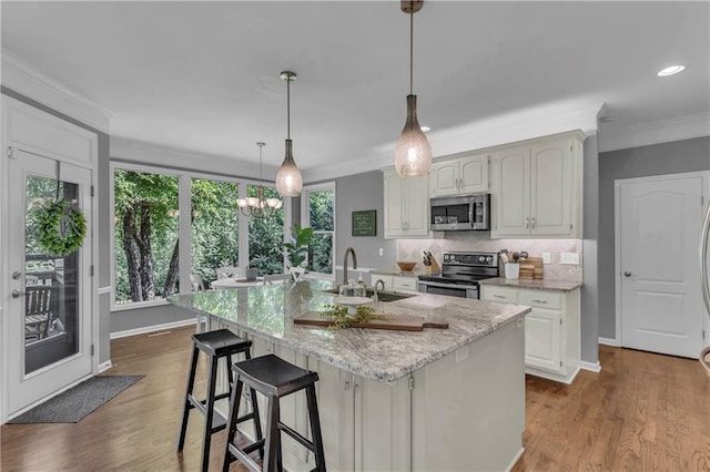 7208 Oakview St, Shawnee, KS 66216 - kitchen featuring appliances with stainless steel finishes, ornamental molding, a sink, an island with sink, and light stone counters