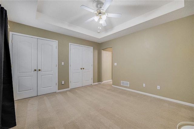 3222 SW Shadow Brook Dr, Blue Springs, MO 64015 - unfurnished bedroom with multiple closets, a tray ceiling, arched walkways, and light carpet