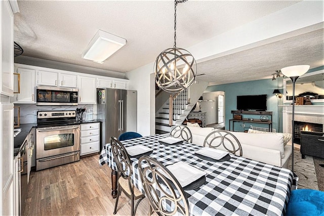 1404 SE Lexington Ave, Lees Summit, MO 64081 - dining space featuring stairway, light wood finished floors, a textured ceiling, a warm lit fireplace, and a chandelier