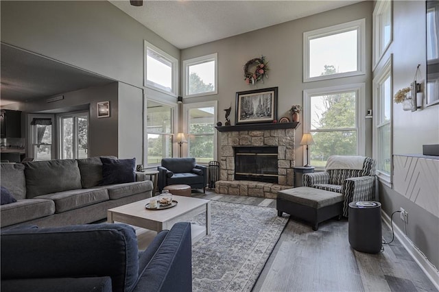 11702 E 246th St, Peculiar, MO 64078 - living room featuring wood finished floors, a stone fireplace, a high ceiling, and a textured ceiling