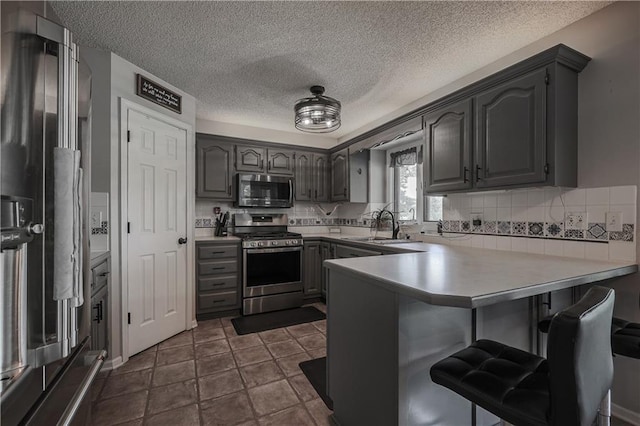11702 E 246th St, Peculiar, MO 64078 - kitchen with appliances with stainless steel finishes, a peninsula, a breakfast bar, decorative backsplash, and a textured ceiling
