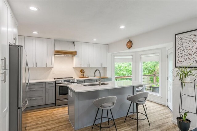 8726 W 104th St, Overland Park, KS 66212 - kitchen featuring appliances with stainless steel finishes, custom exhaust hood, light countertops, gray cabinetry, and a kitchen bar