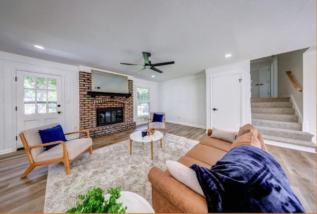 10409 Russell St, Overland Park, KS 66212 - living room featuring wood finished floors, ceiling fan, a brick fireplace, stairway, and baseboards