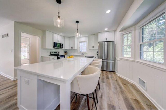 10409 Russell St, Overland Park, KS 66212 - kitchen featuring stainless steel appliances, plenty of natural light, white cabinets, light wood-type flooring, and recessed lighting