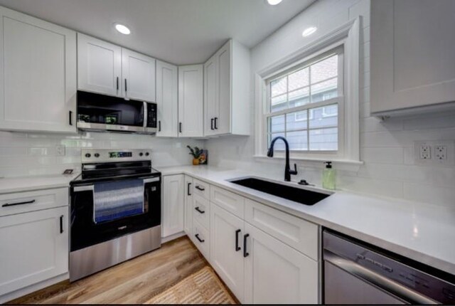 10409 Russell St, Overland Park, KS 66212 - kitchen with stainless steel appliances, a sink, white cabinetry, decorative backsplash, and recessed lighting