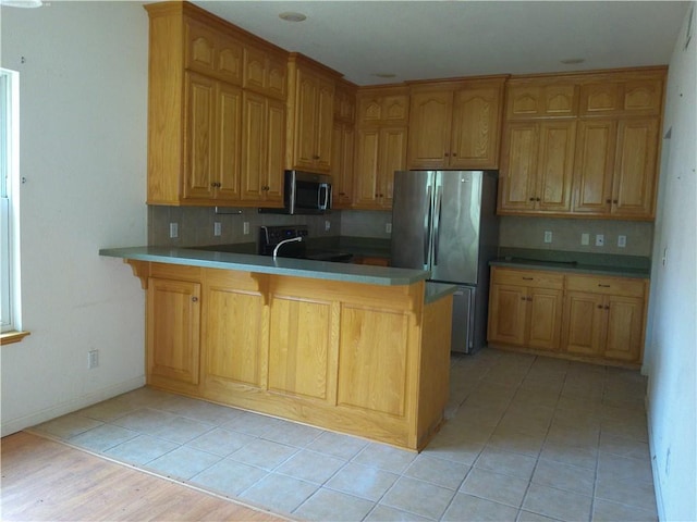 503 W Shawnee St, Paola, KS 66071 - kitchen featuring appliances with stainless steel finishes, decorative backsplash, a peninsula, a kitchen breakfast bar, and baseboards