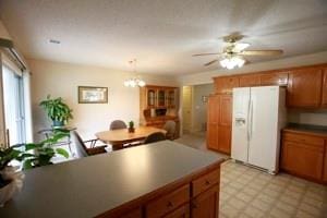 814 Clancy Ct, Raymore, MO 64083 - kitchen with white fridge with ice dispenser, brown cabinets, a chandelier, dark countertops, and a ceiling fan