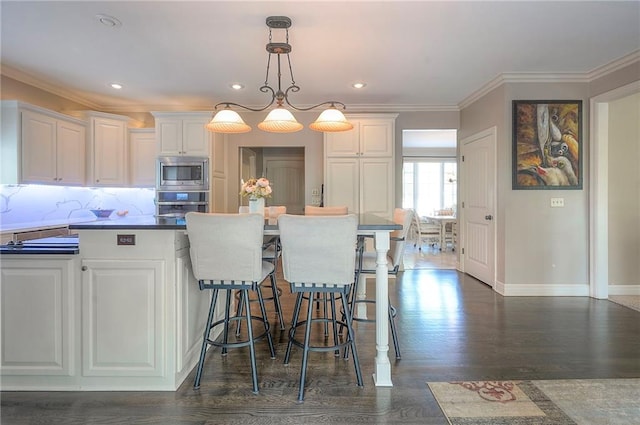 309 E 126th St, Kansas City, MO 64145 - kitchen featuring appliances with stainless steel finishes, white cabinetry, a kitchen breakfast bar, hanging light fixtures, and ornamental molding