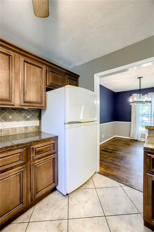 4430 E 107th Ter, Kansas City, MO 64137 - kitchen with freestanding refrigerator, light tile patterned floors, decorative backsplash, a chandelier, and brown cabinetry