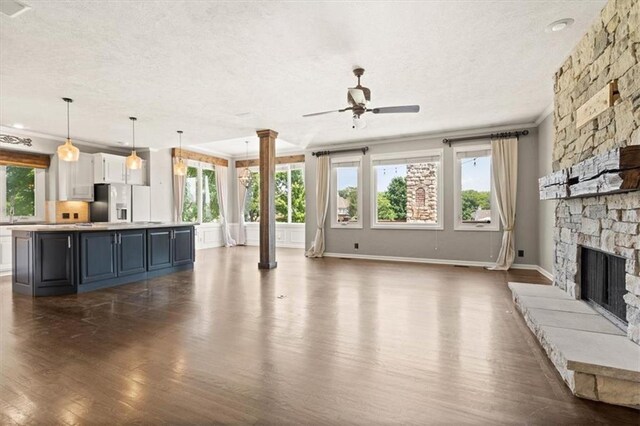 14605 Dearborn St, Overland Park, KS 66223 - unfurnished living room with a textured ceiling, decorative columns, dark wood-style flooring, a ceiling fan, and a fireplace