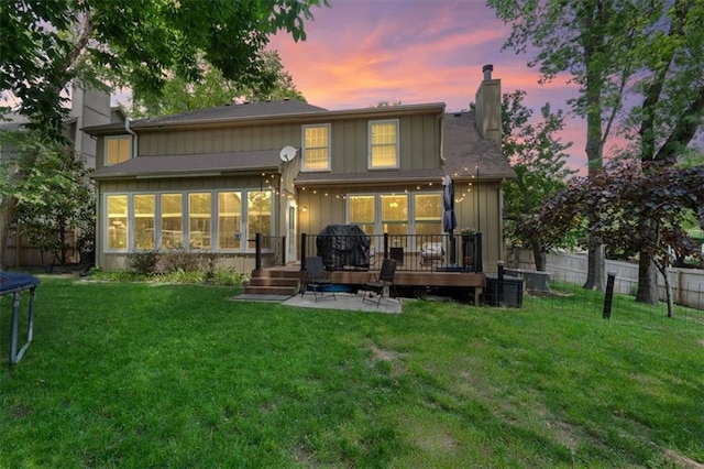 14105 W 115th St, Olathe, KS 66062 - rear view of house featuring a chimney, a trampoline, a wooden deck, board and batten siding, and a sunroom