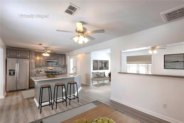 1129 US Highway 50, Centerview, MO 64019 - kitchen featuring stainless steel appliances, a ceiling fan, a kitchen bar, tasteful backsplash, and light wood-type flooring