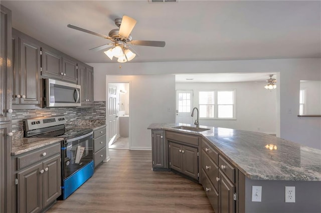 1129 US Highway 50, Centerview, MO 64019 - kitchen with stainless steel appliances, a ceiling fan, an island with sink, decorative backsplash, and dark wood finished floors