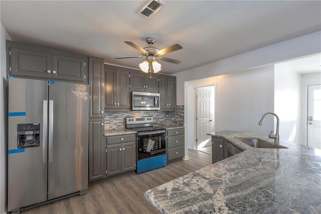 1129 US Highway 50, Centerview, MO 64019 - kitchen with appliances with stainless steel finishes, a ceiling fan, wood finished floors, backsplash, and stone counters
